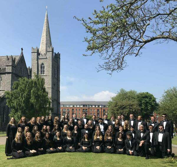The Chorale, dressed in black formal wear, poses on a grassy lawn in front of St. Patrick's Cathedral in Dublin.