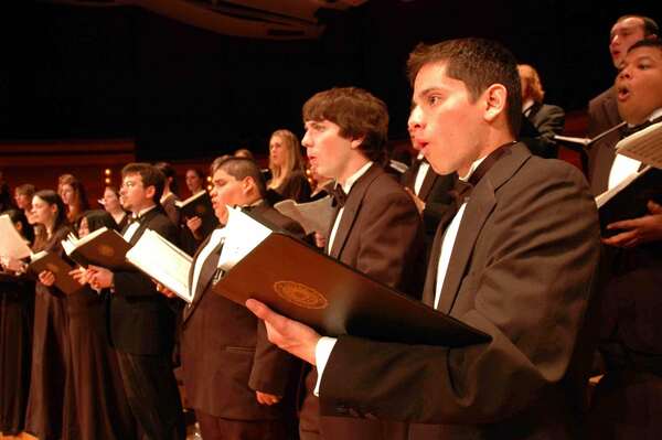 Members of the Chorale, wearing black formal wear and holding music binders, sing during a concert performance.